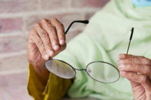 Older adult reading near a window with glasses, soft daylight, and an eye chart in the background